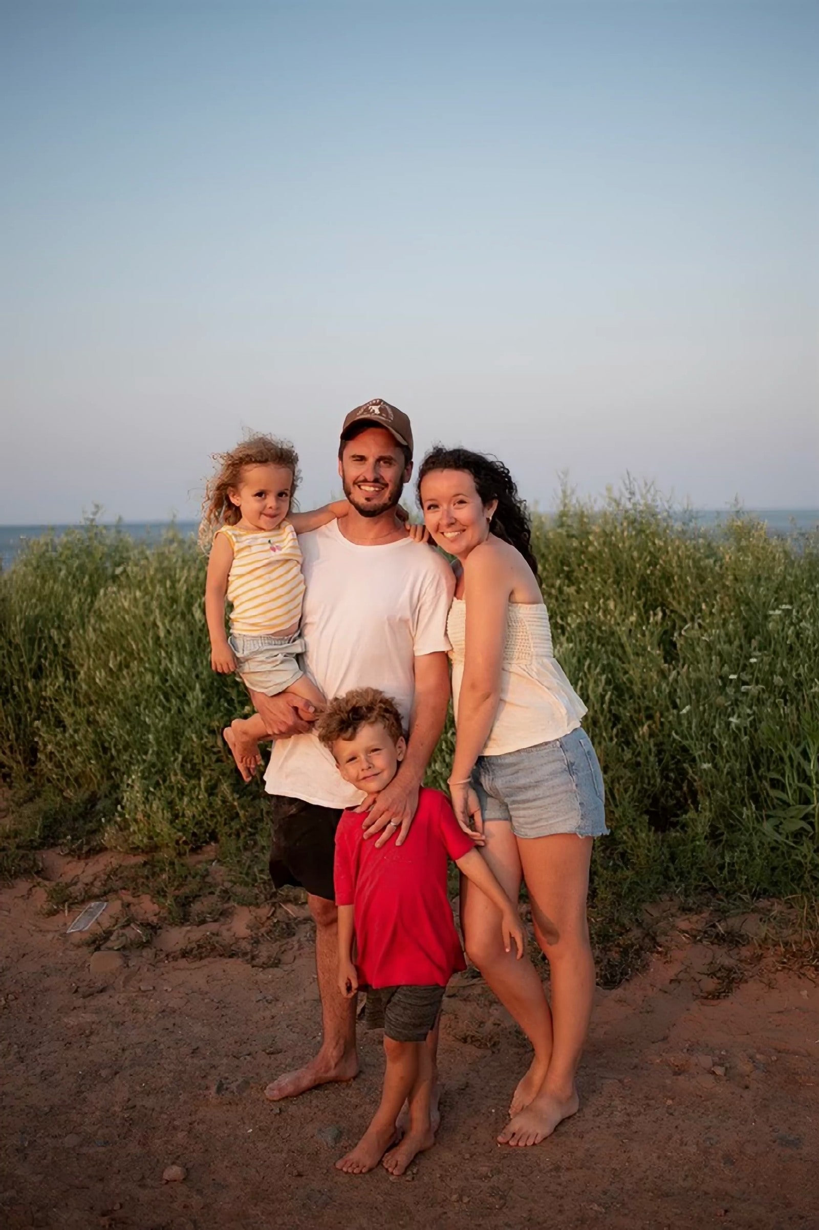 Joseph Poirier avec sa conjointe et leurs deux enfants, debout dans les herbes au bord de la mer